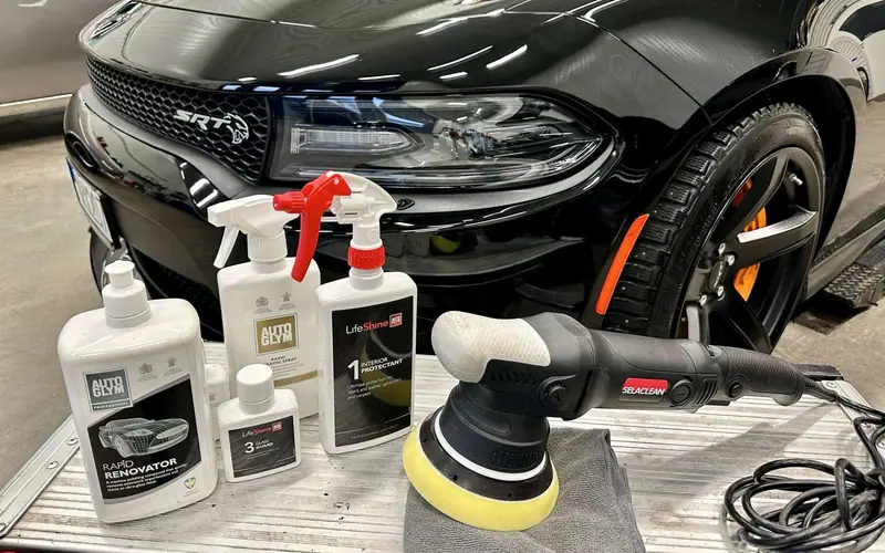 Polermaskin och polermedel från Autoglym framför en blank svart bil i verkstaden.