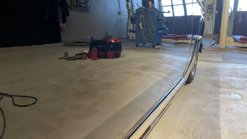 Närbild längs sidan på en blankpolerad bil där verkstadsgolvet och fönstren speglas i lacken.