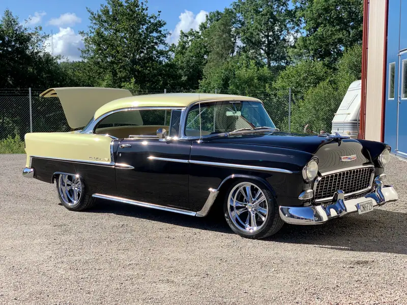 Svart och gul Chevrolet Bel Air med öppen bagagelucka på en grusplan en sommardag.