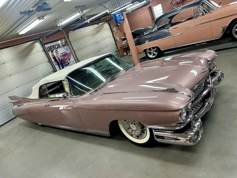 Rosa Cadillac cabriolet från 50-talet med vit sufflett och höga stjärtfenor i kundens garage.