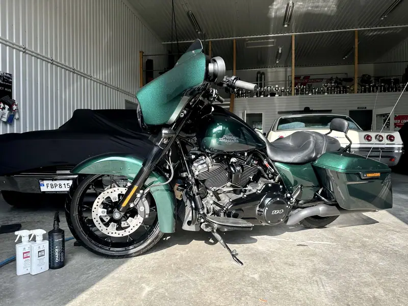 Grön Harley-Davidson Street Glide med blank metalliclack i ett garage, bredvid flaskor med Autoglym-produkter.