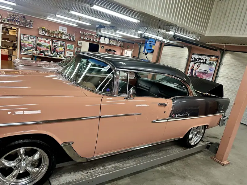 Laxrosa och grå Chevrolet Bel Air på en lyft i kundens garage, med blanka kromlister.