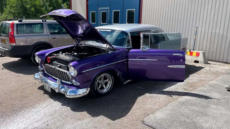Lila Chevrolet Bel Air med öppen motorhuv och öppen dörr utanför en verkstad.