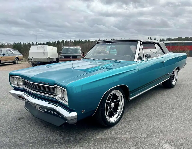 Turkos amerikansk cabriolet med svart sufflett på en grusplan.