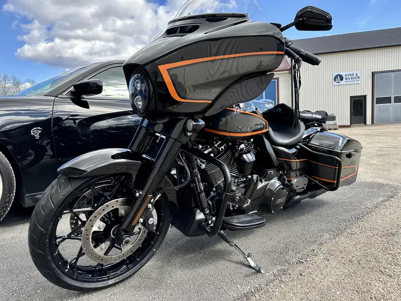 Svart Harley-Davidson Street Glide med orange ränder på kåpan, fotograferad snett framifrån i solsken.