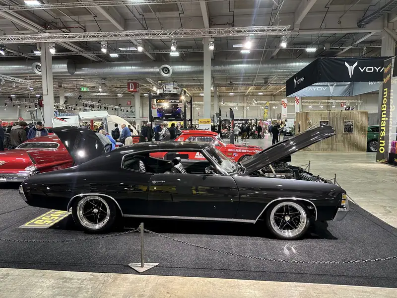 Blanksvart Chevrolet Chevelle med öppen motorhuv från sidan i en monter på en bilmässa.