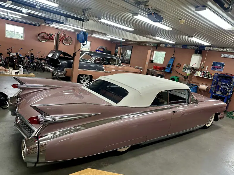 Den rosa Cadillac-cabrioleten snett bakifrån med höga stjärtfenor och vit sufflett.