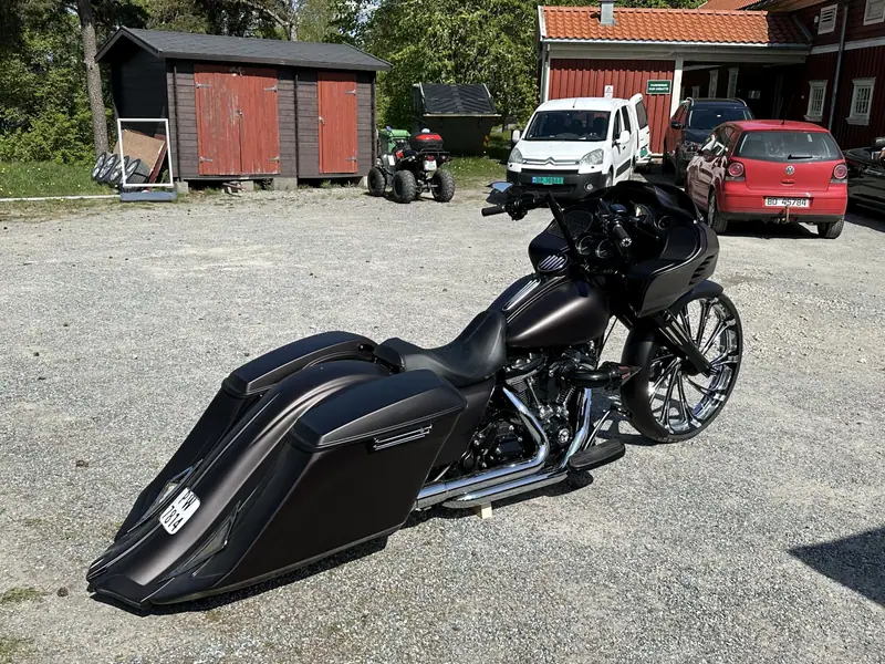 Mattsvart bagger-motorcykel med långa sidoväskor och stort kromat framhjul på en grusplan.