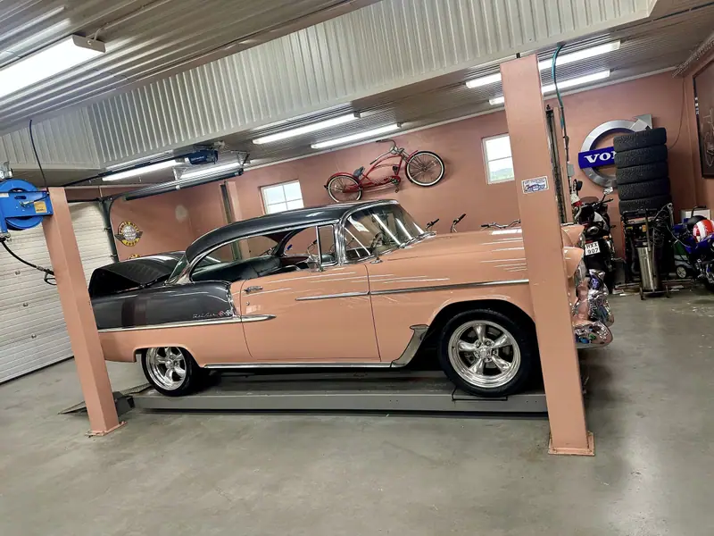 Chevrolet Bel Air från sidan på en lyft i kundens garage, med en röd cykel och en Volvoskylt på väggen.