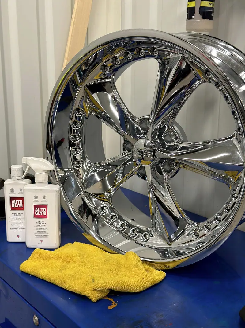 Kromad fälg som speglar omgivningen, bredvid flaskor med Autoglym-produkter och en gul mikrofiberduk.