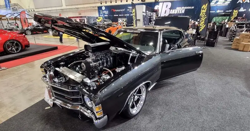 Den svarta Chevrolet Chevelle med öppen motorhuv och kromad kompressor på motorn i en mässhall.