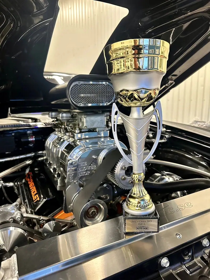 Kromad kompressor på motorn i en svart bil, med en pokal på motorhuven.