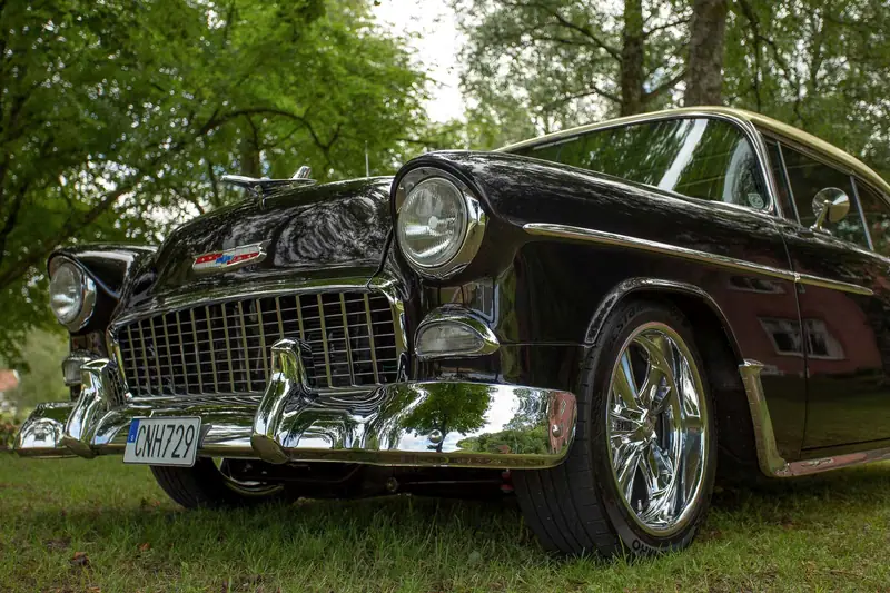 Blank svart Chevrolet Bel Air från 1955 med kromad grill och stötfångare, fotograferad nerifrån i gräset.