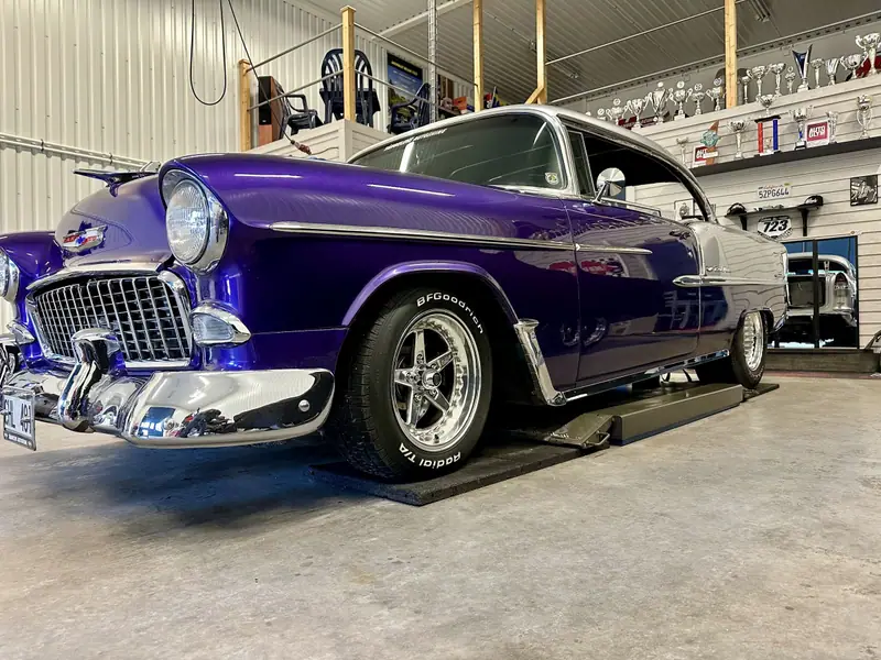 Lila Chevrolet Bel Air med silverfärgat tak och kromad front på en lyft i verkstaden.