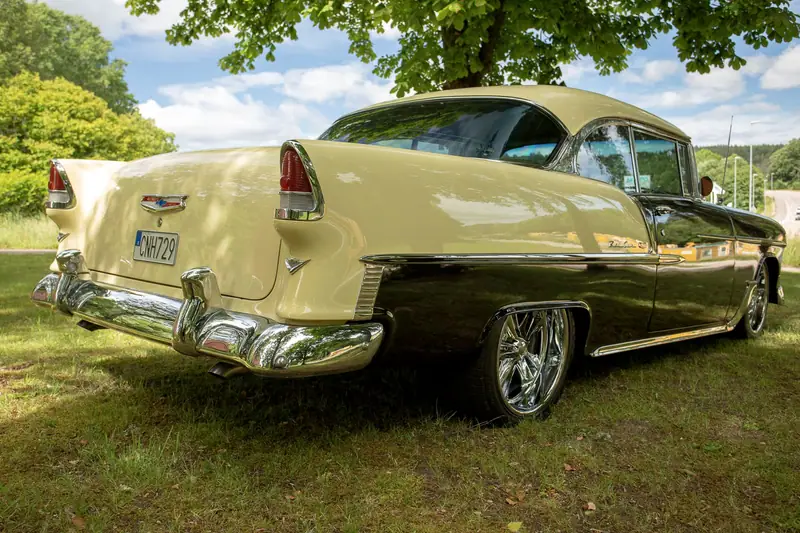 Chevrolet Bel Air från 1955 i svart och gräddgult, fotograferad snett bakifrån på en gräsmatta en solig dag.