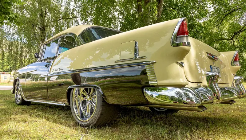 Chevrolet Bel Air från 1955 i svart och gräddgult, fotograferad lågt från sidan, med träden som speglas i lacken och kromen.