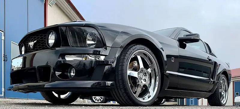Svart Ford Mustang med kromade fälgar, fotograferad lågt framifrån framför verkstaden.