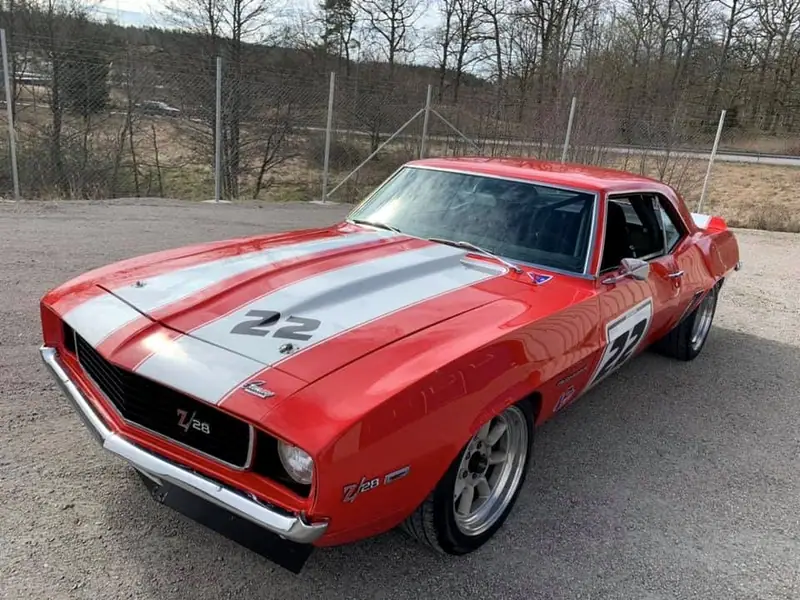 Röd Chevrolet Camaro med vita racingränder och startnummer 22 på en grusplan.