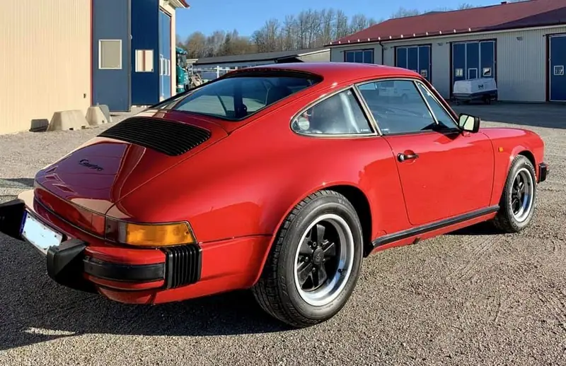Röd klassisk Porsche 911 fotograferad snett bakifrån utanför verkstaden.