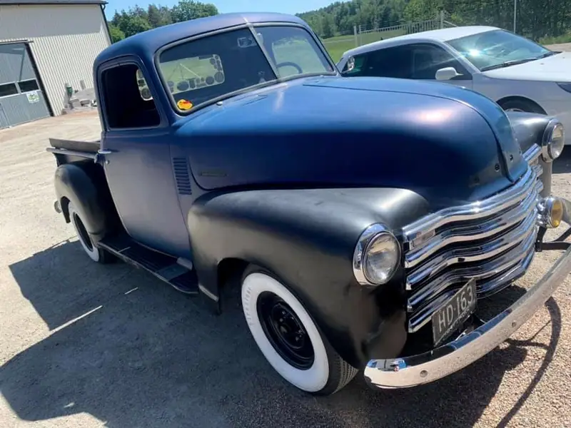 Klassisk Chevrolet-pickup i blått och svart med vita däcksidor, fotograferad utomhus snett framifrån.