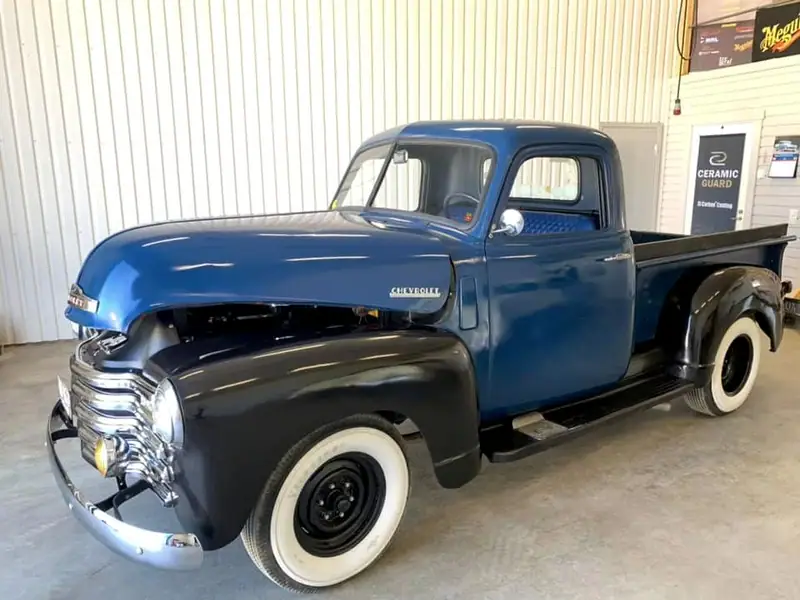 Klassisk Chevrolet-pickup i blått och svart med vita däcksidor i verkstaden.