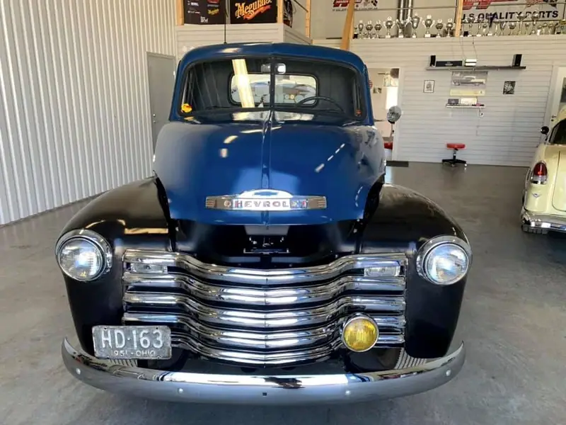 Kromad grill och runda strålkastare på en klassisk Chevrolet-pickup, rakt framifrån i verkstaden.