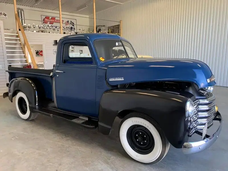 Klassisk Chevrolet-pickup i blått och svart från sidan i verkstaden, med pokaler på hyllan bakom.