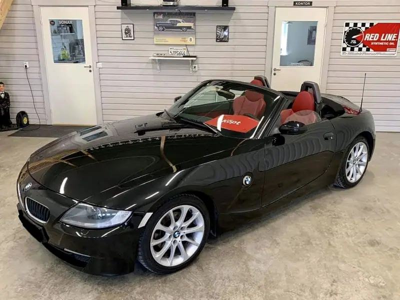 Svart BMW Z4 cabriolet med nedfälld sufflett och röd inredning i verkstaden.