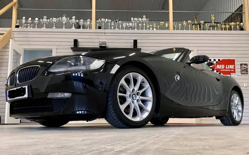 Svart BMW Z4 fotograferad lågt från sidan i verkstaden, med pokaler på hyllan bakom.