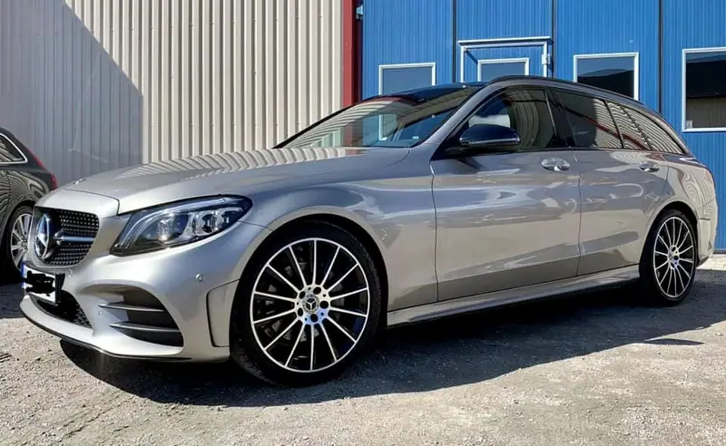 Silverfärgad Mercedes-Benz C-klass kombi framför verkstadens blå portar.