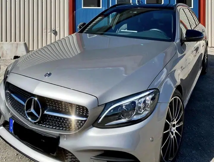 Front och strålkastare på en silverfärgad Mercedes-Benz C-klass, fotograferad snett ovanifrån.