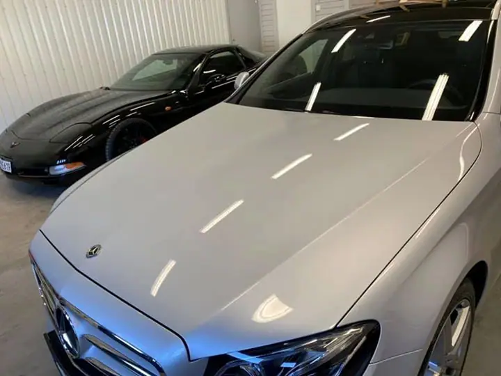 Närbild på motorhuven på en silverfärgad Mercedes där taklamporna speglas, med en svart sportbil i bakgrunden.