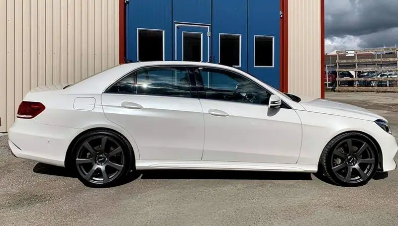 Vit Mercedes-Benz E-klass sedan från sidan framför verkstadens blå portar.