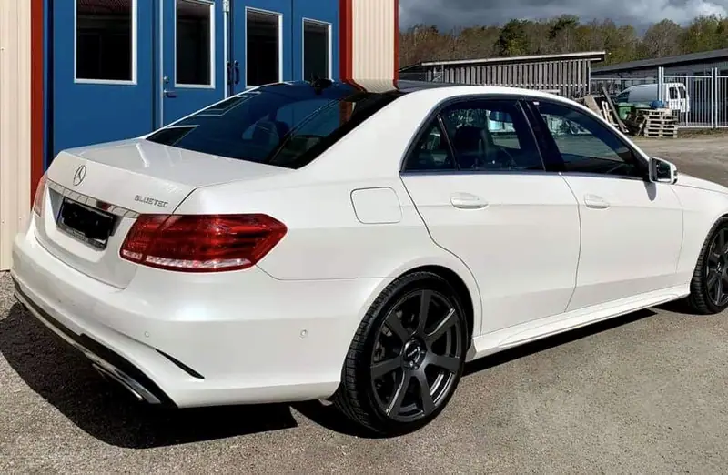 Vit Mercedes-Benz E-klass sedan snett bakifrån utanför verkstaden.