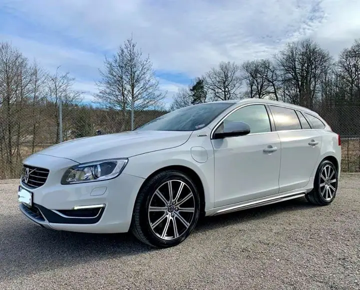 Vit Volvo V60 med mörka fälgar på en grusplan en solig dag.