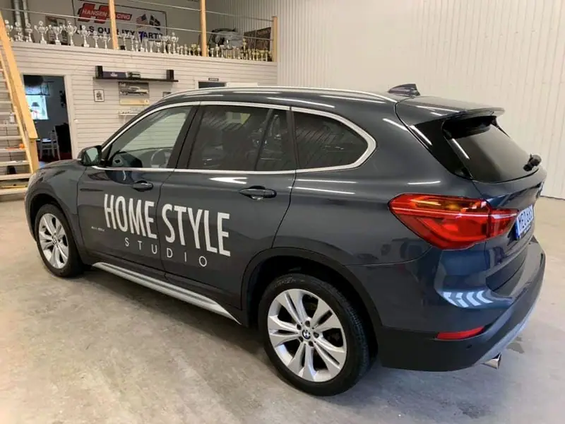 Grå BMW X1 med dekoren Home Style Studio i verkstaden, snett bakifrån.