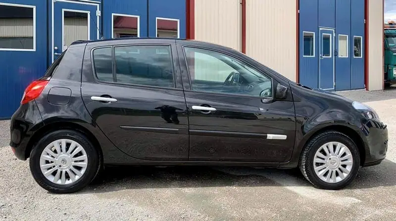 Svart Renault Clio från sidan framför verkstadens blå portar.